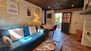 A cozy room with a stone wall, a blue sofa, a wooden table with a placemat, and a sign reading "FLEURS DE MÃR". - La Terrasse de Sacha | House with Terrace & Fireplace | 4 Guests (Honfleur)