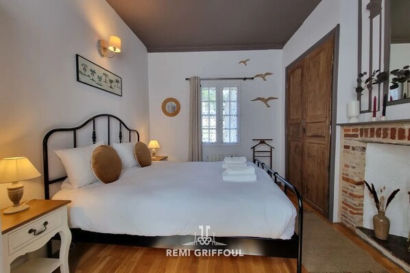 Quarto com cama, mesas de cabeceira, espelho, lareira e janela com cortinas.