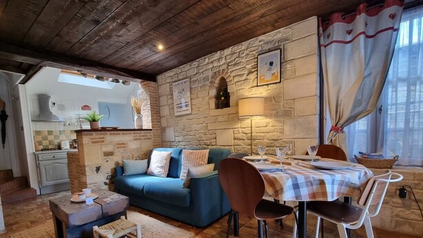A cozy living room with a blue sofa, a dining table with chairs, and a kitchen in the background. - La Terrasse de Sacha | House with Terrace & Fireplace | 4 Guests (Honfleur)