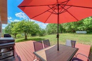 Une terrasse en bois avec un parasol rouge, un barbecue et une table entourée de chaises.