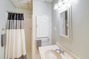 Une salle de bain avec un rideau de douche, un porte-serviettes, un lavabo avec un miroir et une porte.
