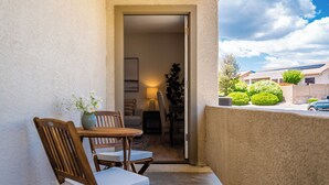 Een balkon met een houten tafel en stoelen, een bloempot en uitzicht op een woongebied met groen en een auto.