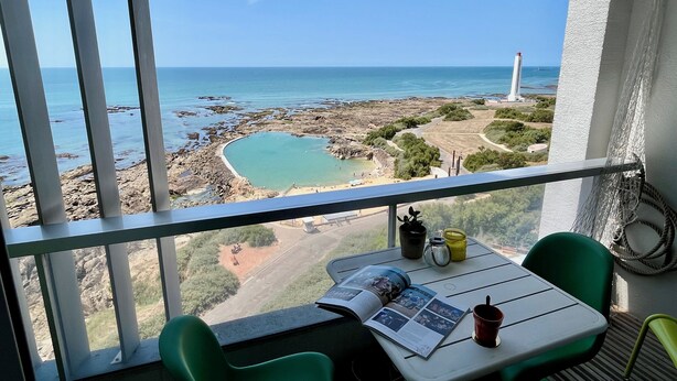 Ein Balkon mit Tisch, Stühlen und Blick auf das Meer und einen Leuchtturm.