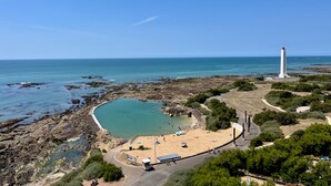 Eine Küstenlandschaft mit Leuchtturm, felsigem Strand, klarem Wasser und einem kleinen Pool.