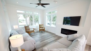 A spacious living room with a large window, a ceiling fan, a flat-screen TV, and a fireplace. - 6 BR Townhome Oceanvws Rooftop Deck Pool (Panama City Beach)