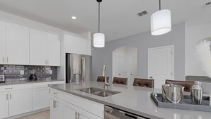 A modern kitchen with white cabinets, stainless steel appliances, and a central island with seating. - 6BR Villa with Pool & Games Room, Near Disney (Davenport)