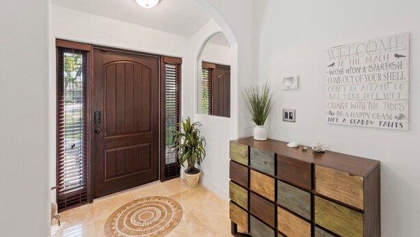 A hallway with a wooden door, a potted plant, a decorative wall sign, and a wooden console with drawers. - Marco Island Family Retreat  (Marco Island)