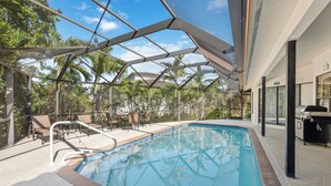 An indoor pool area with a glass ceiling, lounge chairs, and a barbecue setup. - Marco Island Family Retreat  (Marco Island)