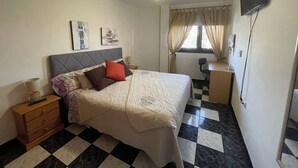 A bedroom with a bed, a nightstand, a desk, a chair, a television, and a ceiling fan. - Vistamar La Caleta 2 (La Caleta)