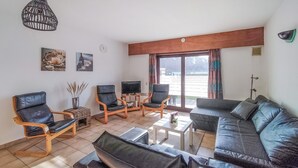 En stue med sofa, to lænestole, fjernsyn og et stort vindue.