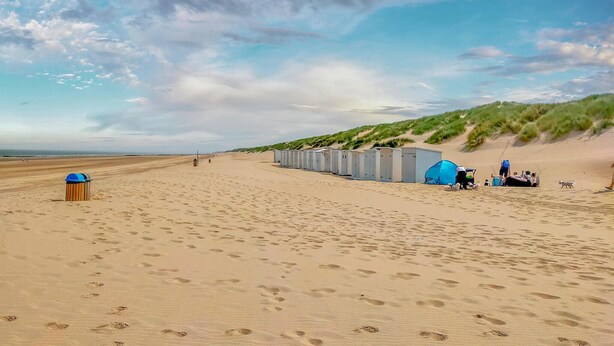 En strand med transportable toiletter og telte, en skraldespand og fodspor i sandet.