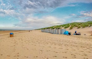 A beach with portable toilets and tents, a trash bin, and footprints in the sand. - Amazing apartment in Bredene (Bredene)