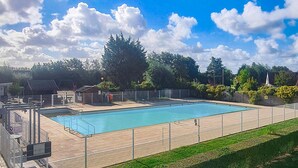 Et rektangulært pool med gelænder og træterrasse, omgivet af træer og en blå himmel.