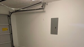 Un garage pulito e vuoto con pavimento in cemento, una porta metallica e un lampadario a soffitto.
