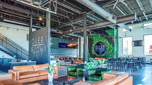 Ein großzügiger Lounge-Bereich mit Ledersofas, einer Bar und einem großen Schild mit der Aufschrift 'OVER FLOW'.