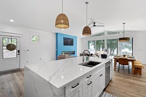 Una cocina moderna con encimera de mármol blanco, un lavaplatos integrado y una zona de comedor con sillas y mesa de madera.