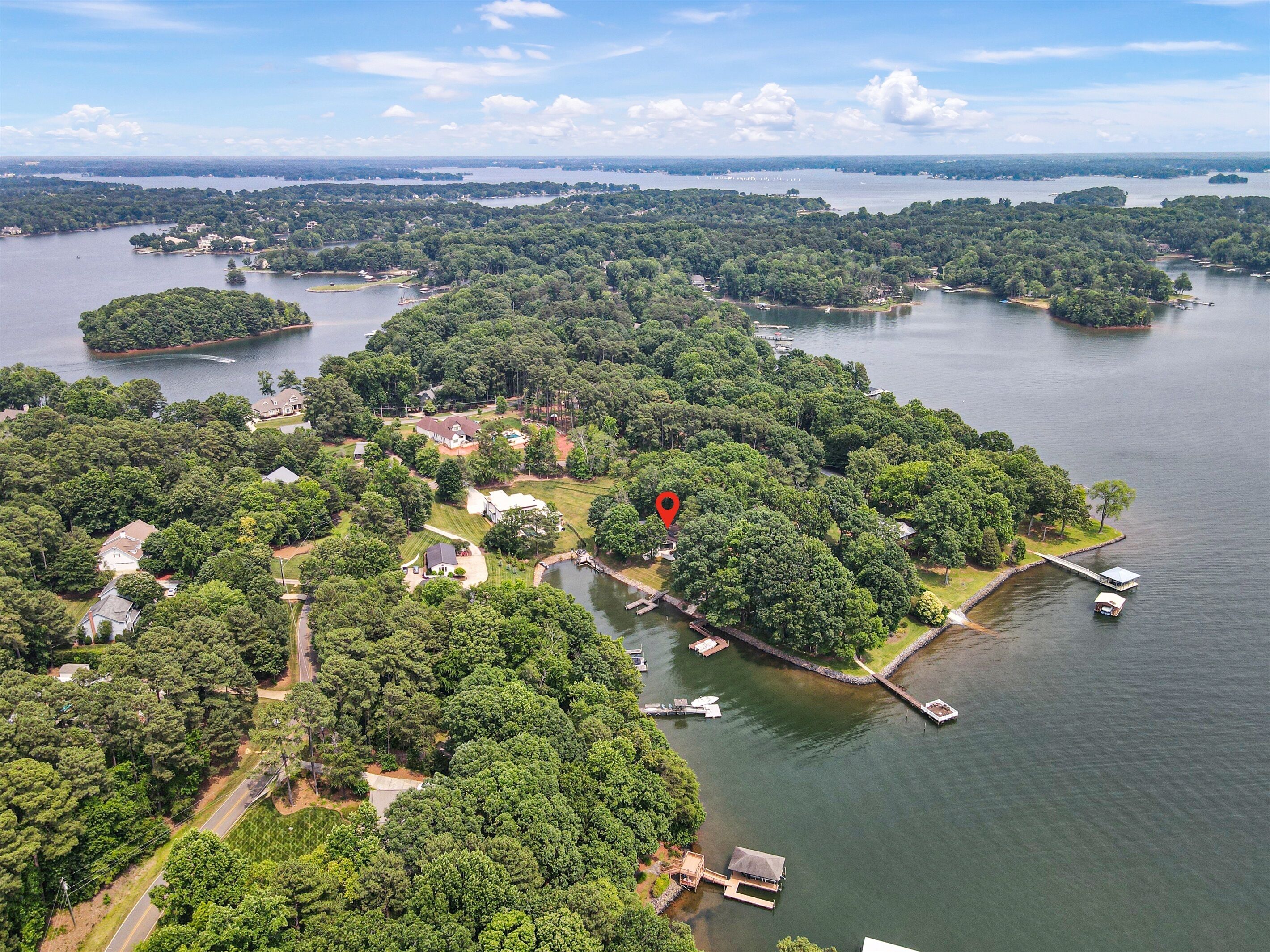 Une vue aérienne d’une propriété au bord du lac, avec plusieurs quais, des bateaux et un marqueur rouge indiquant un emplacement précis.
