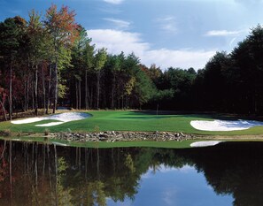 Un campo de golf con búnkeres de arena, un estanque y árboles reflejados en el agua.