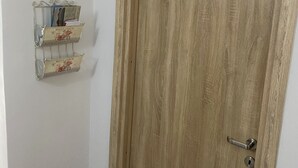 Eine Holztür mit einem Metallbeschlag und Schlüsselloch, daneben ein Metallregal mit Dekorationen an der Wand.