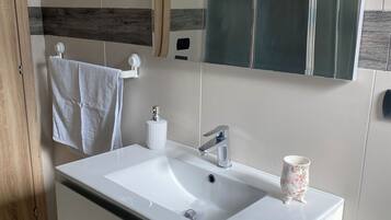 A modern bathroom with a white sink, a mirror, and a wooden door.