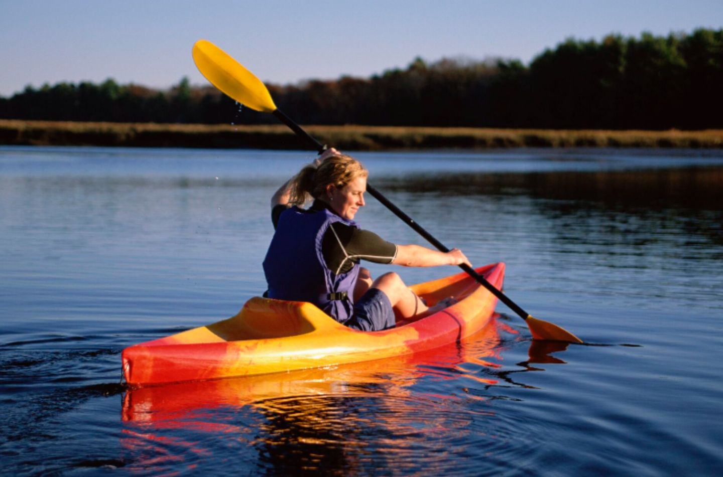 A person kayaking on a calm lake with a forest in the background.