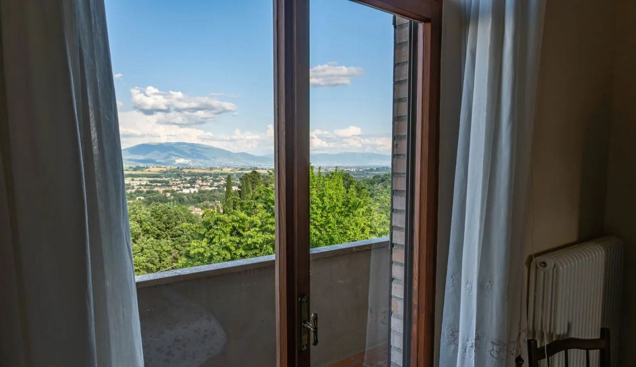 A room with a view of a green landscape and mountains.