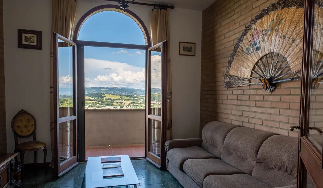 A room with a balcony, a sofa, a table, and a decorative fan.