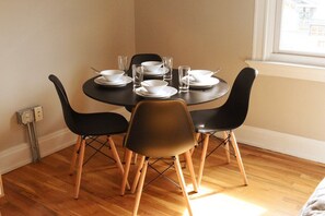 A dining area with a round table set for four, surrounded by black chairs with wooden legs.