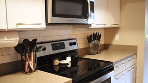 Una cocina con estufa negra, un microondas encima y un portavasos para cuchillos en la encimera.