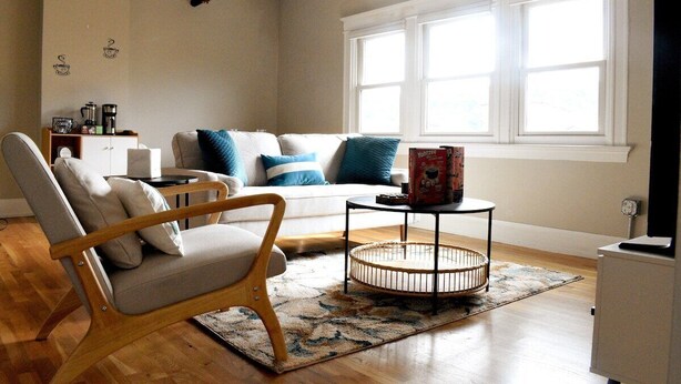 Una sala de estar con una silla de madera, un sofá con cojines azules, una mesa de centro y un mueble para televisor.
