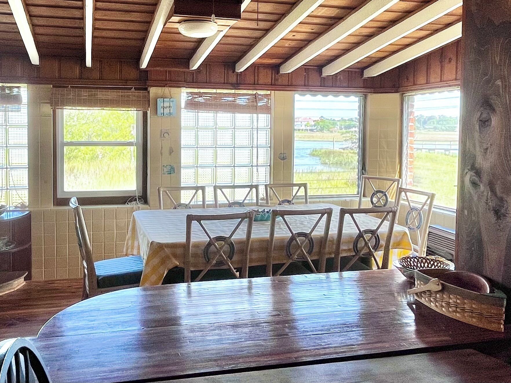 A rustic dining area with a wooden table and chairs, large windows with views of a field, and a 'Happy Place' sign.