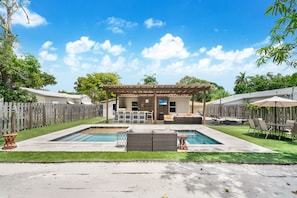 Un patio trasero con piscina, mobiliario exterior y una pérgola.