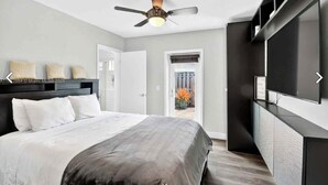 Een slaapkamer met een bed, een plafondventilator, een televisie en een schuifdeur naar een balkon.