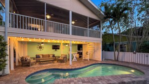 A pool area with a covered patio, outdoor furniture, and a view of the house. - Coral Cove: Walk to the Beach! Heated pool! Prime North End! (Anna Maria)