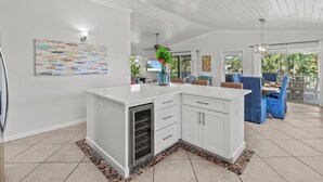 A modern kitchen with white cabinetry, a built-in oven, and a dining area with blue chairs. - Coral Cove: Walk to the Beach! Heated pool! Prime North End! (Anna Maria)