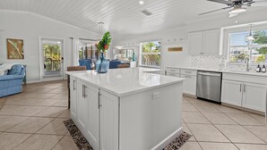 A spacious kitchen with a central island, white cabinetry, and a ceiling fan. - Coral Cove: Walk to the Beach! Heated pool! Prime North End! (Anna Maria)