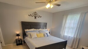 A bedroom with a wooden bed, a ceiling fan, a nightstand, and a window with curtains. - Family-friendly, Less than 5 minutes from Kings Bay, water park huge backyard.
 (St. Marys)