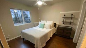 Ein Schlafzimmer mit Bett, Deckenventilator, Fenster mit Blick auf Bäume und Heizkörper.