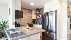 Une cuisine moderne équipée d’un réfrigérateur en acier inoxydable, d’un four encastré et d’un plan de travail sur lequel se trouve une bouteille de champagne.