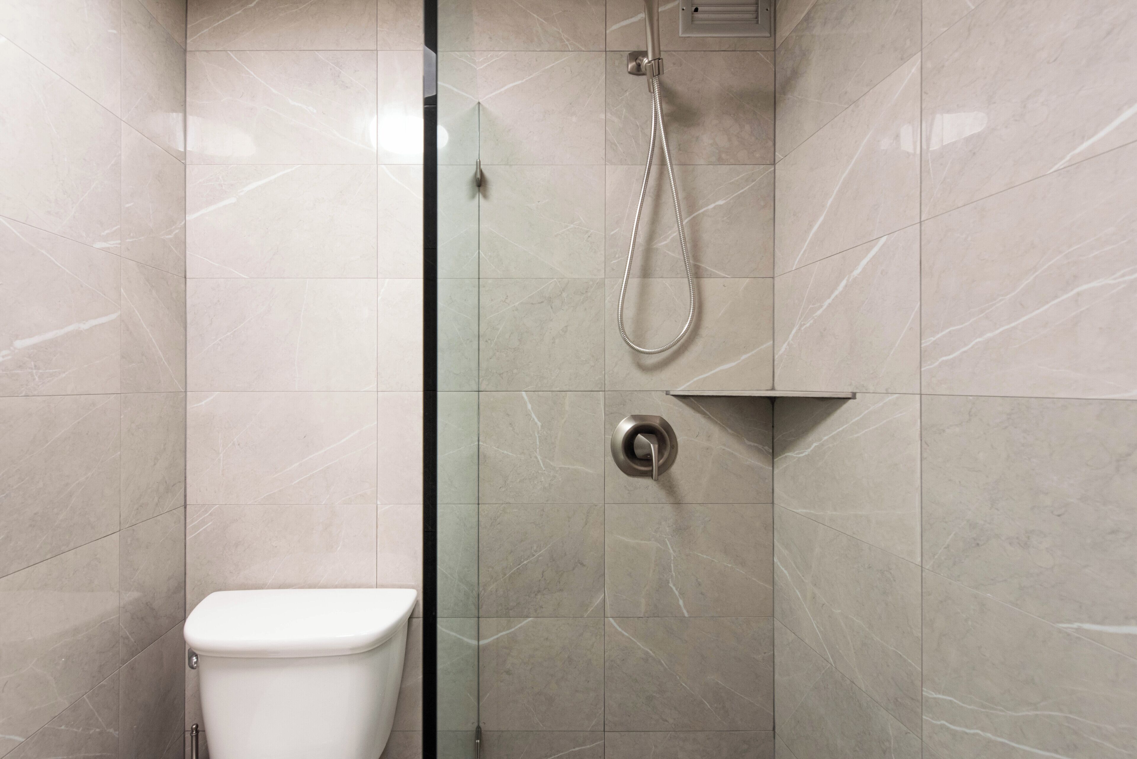 Une salle de bain moderne équipée de toilettes, d’une douche avec un pommeau de douche amovible et d’un panneau de commande fixé au mur.