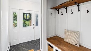 Un couloir avec une porte blanche, un banc en bois doté d’un coussin et un porte-manteau fixé au mur.