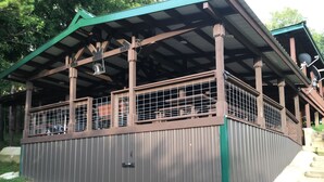 Un espacio al aire libre techado con techo de metal, vigas de madera y barandilla.