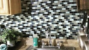 Una cocina con salpicadero de azulejos, pileta de acero inoxidable, armarios de madera y una planta en maceta.