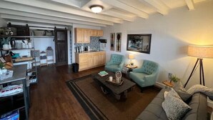 Amplia sala de estar con una cocina al fondo, una mesa de centro, dos sillones y un sofá.