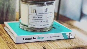 Una vela etiquetada 'Zen Moss' sobre un libro azul verdoso titulado 'Quiero dormir' de Harriet Griffith.