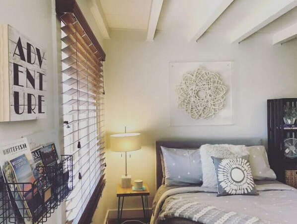 Une chambre à coucher avec un lit, un élément décoratif fixé au mur et une fenêtre avec des stores.