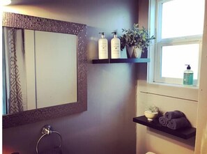 Une salle de bain avec un grand miroir, un porte-serviettes, une étagère avec des articles de toilette et une fenêtre.