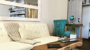 Een witte bank met een plaid, een blauwgroene fauteuil en een houten salontafel met een boek en een plant.