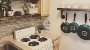 Een keuken met een witte kookplaat, houten kastjes en een achterwand van baksteen. Er hangen pannen aan de muur en een bord met de tekst 'Eat Well Travel Clean'.