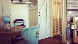 Een kamer met een bureau, een blauwe stoel, een hanglamp en een schuifdeur naar een badkamer.